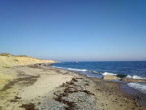 Une plage avec un ciel dégagé, une mer calme et une côte rocheuse.