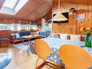 A cozy cabin interior with a wooden ceiling, a sofa, a dining table, and a bed with a floral bedspread.
