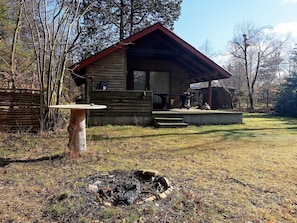 A rustic cabin with a wooden exterior, a porch, and a fire pit in the foreground.