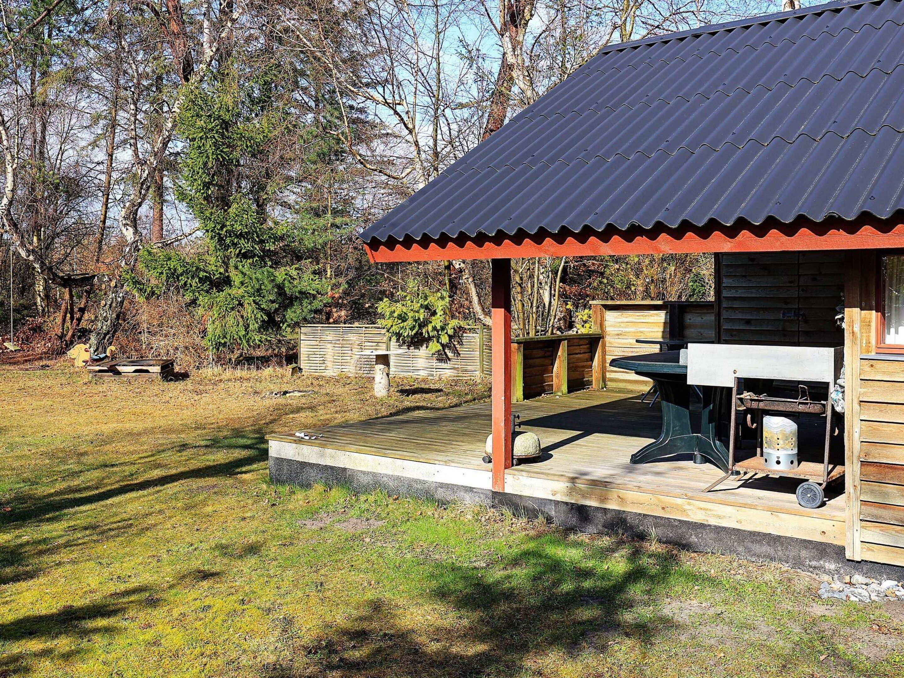 A wooden cabin with a metal roof, a deck, and a barbecue area.