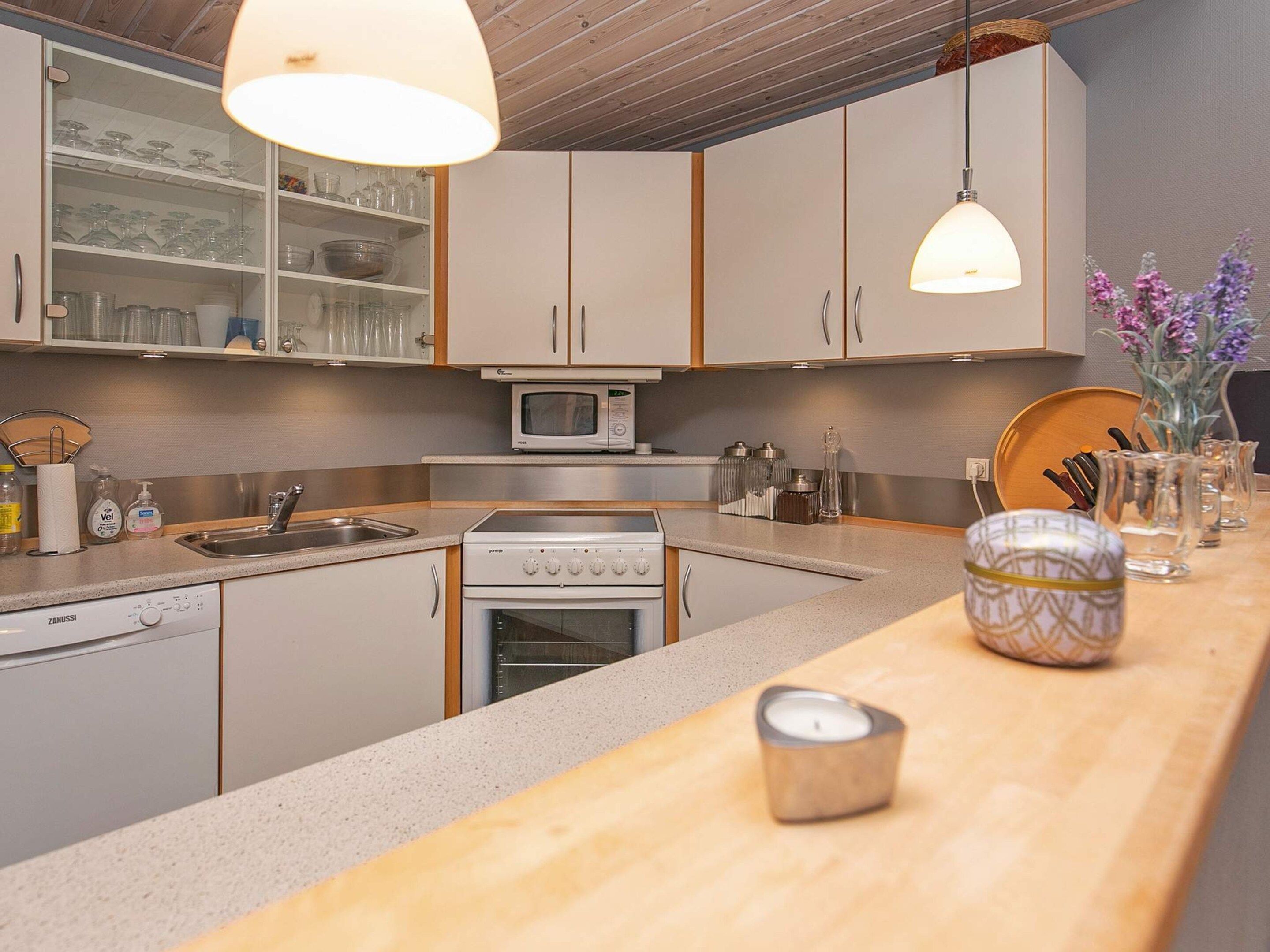 A modern kitchen with wooden cabinets, a built-in microwave, a stove, and a sink. There are hanging pendant lights and a vase with flowers on the counter.