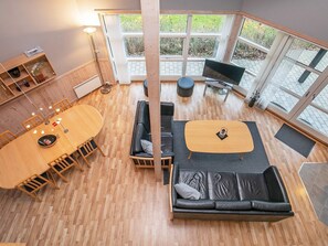 A modern interior with a wooden dining table, black leather sofa, and a TV.
