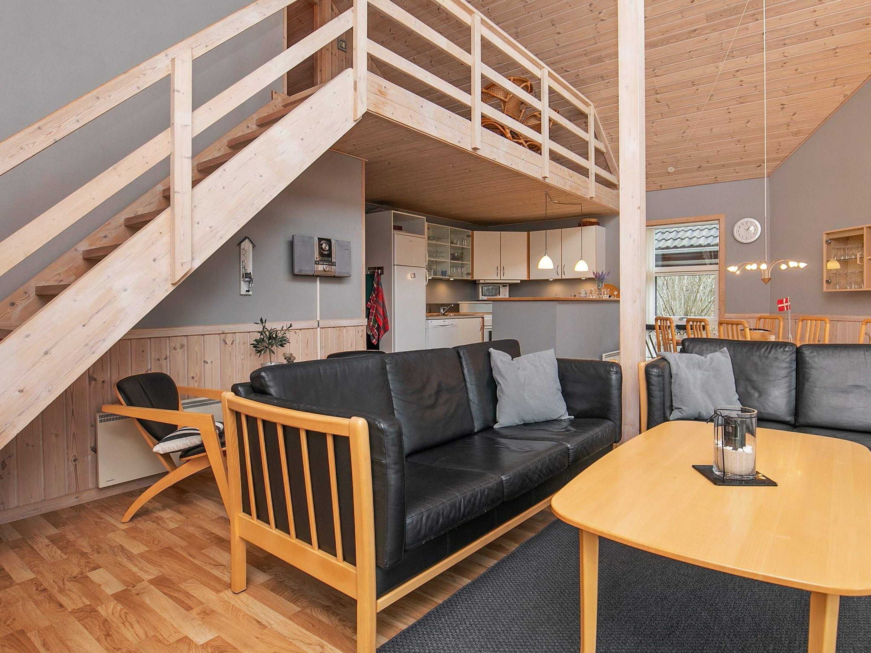 Un intérieur moderne avec un escalier en bois, un canapé en cuir noir, une table à manger en bois et un coin cuisine.