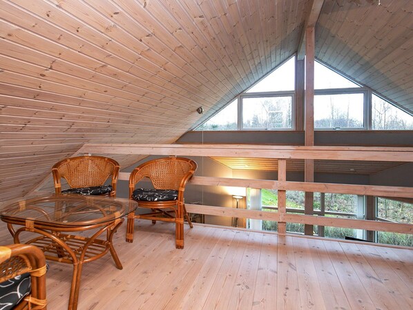 A wooden deck with wicker chairs and a glass table, overlooking a forested area.