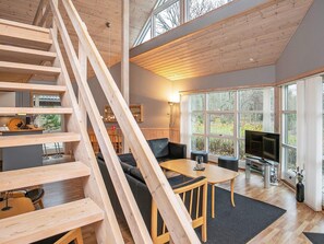 A modern interior with a wooden staircase, a living area with a sofa, a dining table, and a TV.