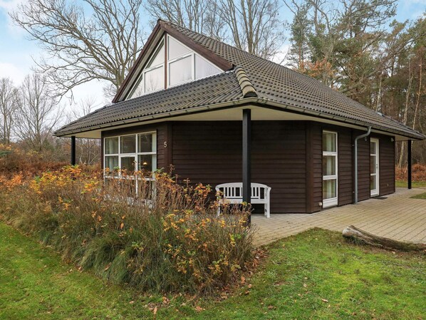 A two-story wooden house with a sloped roof, a porch with two white chairs, and a number '5' on the side.