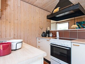 A compact kitchen with wooden walls, a stove, a coffee maker, and a red pot on the counter.