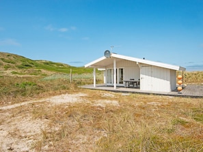 A coastal building with a covered patio, a satellite dish, and a sandy landscape.