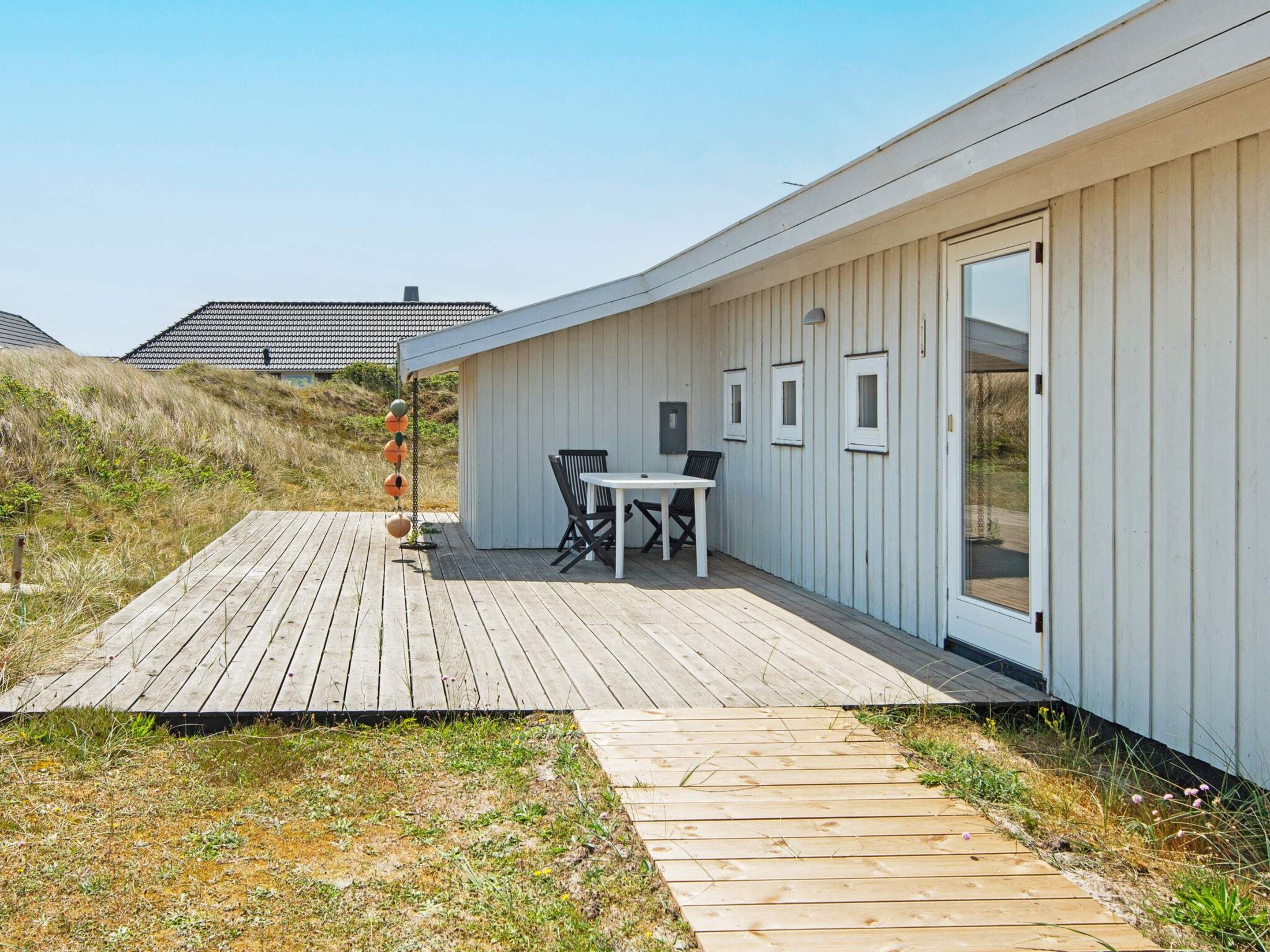 A modern building with a wooden deck, a table and chairs, and a door with windows.