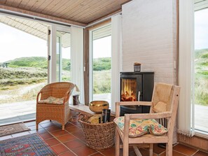 A cozy room with a fireplace, wicker chairs, and a view of the beach.
