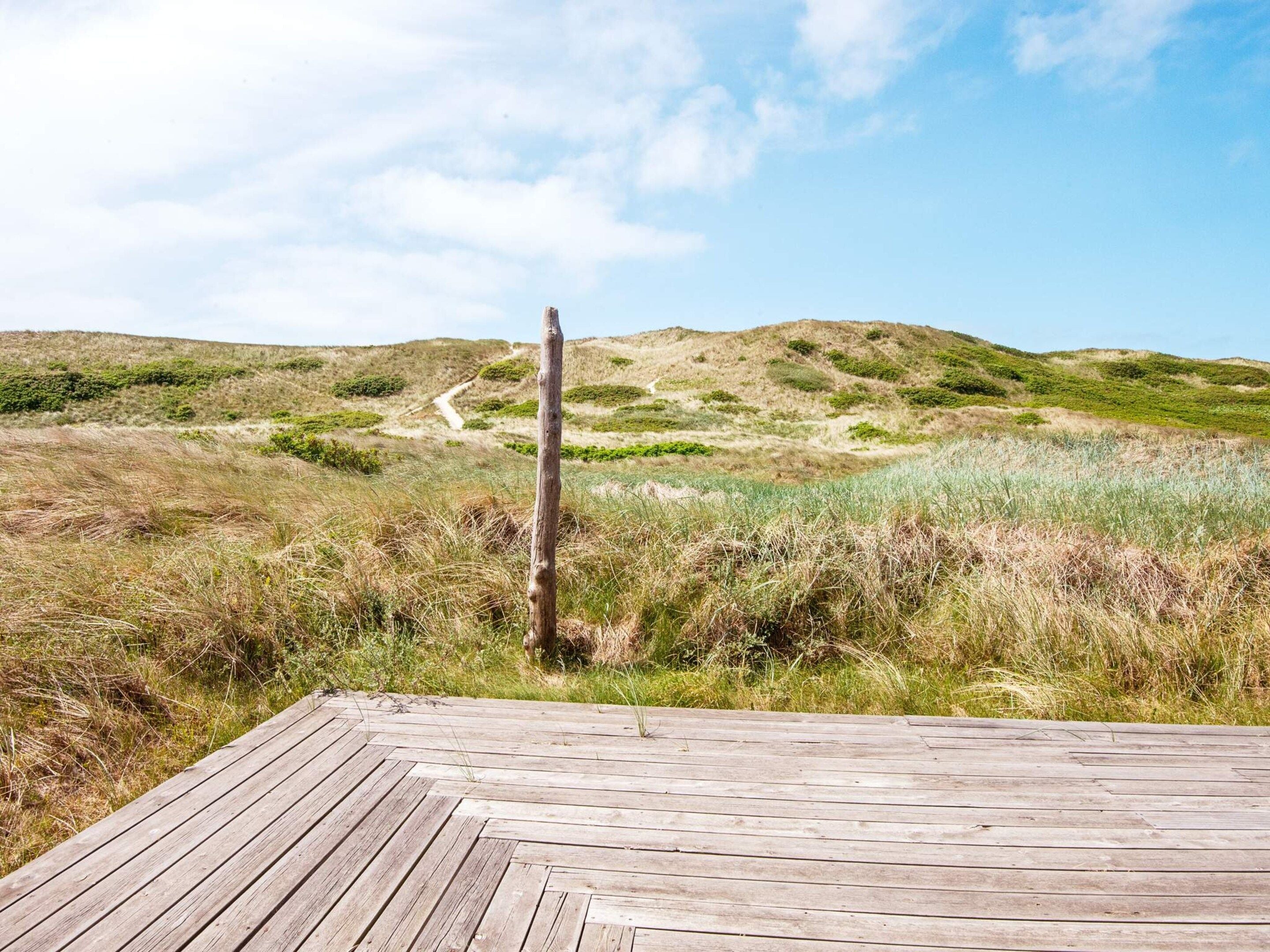 A wooden deck with a clear view of a grassy landscape and a dirt path leading uphill.