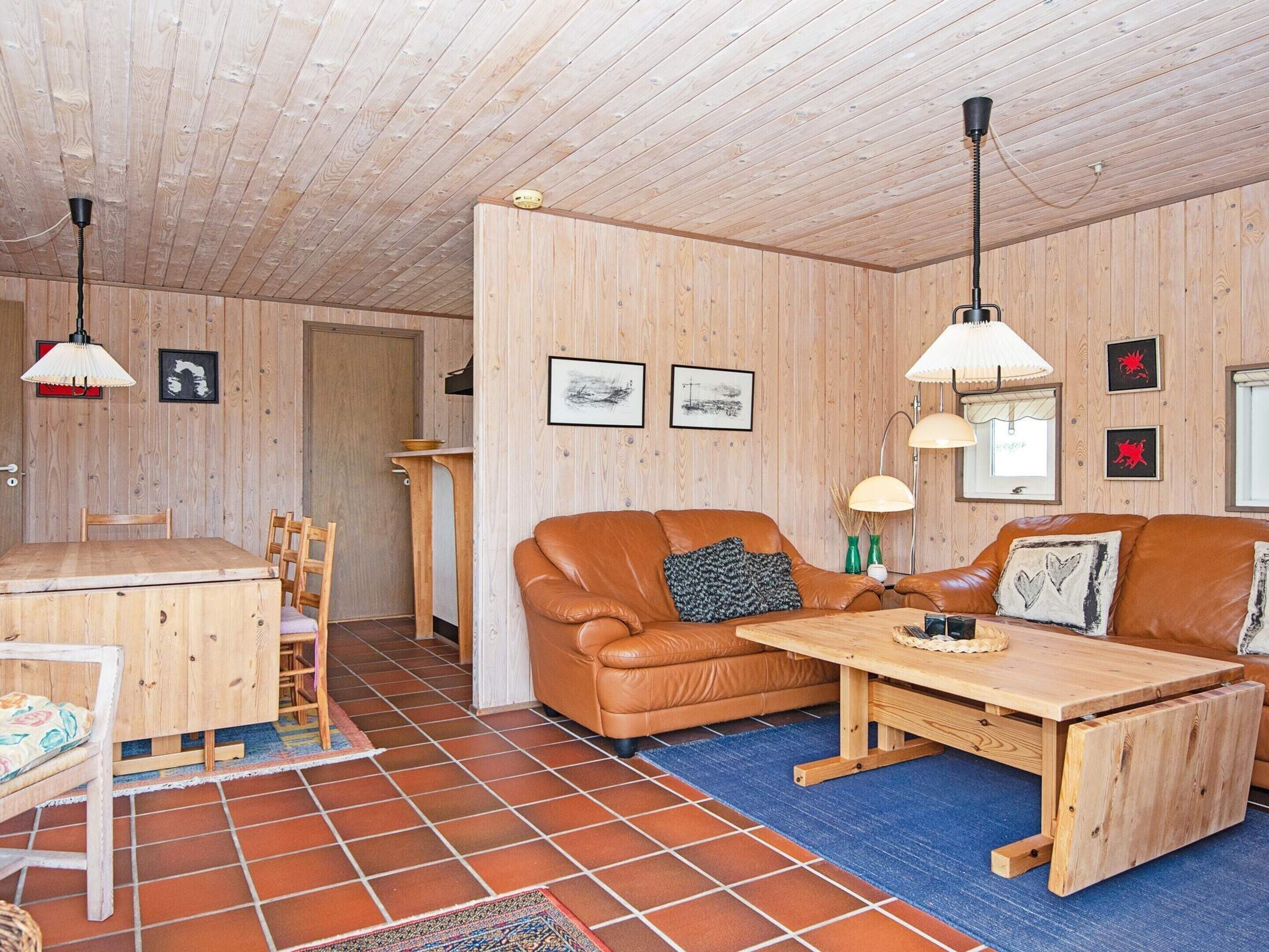 A cozy room with a wooden ceiling, a brown leather sofa, a wooden dining table, and a blue rug.