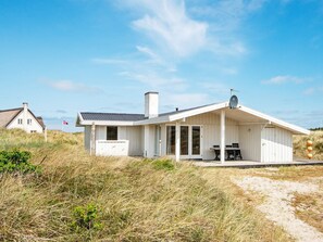 Ett vitt strandhus med en täckt uteplats, en satellitmottagare och en flagga.