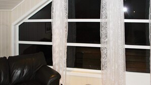 A room with a black leather sofa, a radiator, and lace curtains on a window. - 5 Person Holiday Home in Selsoyvik (Rodoy)