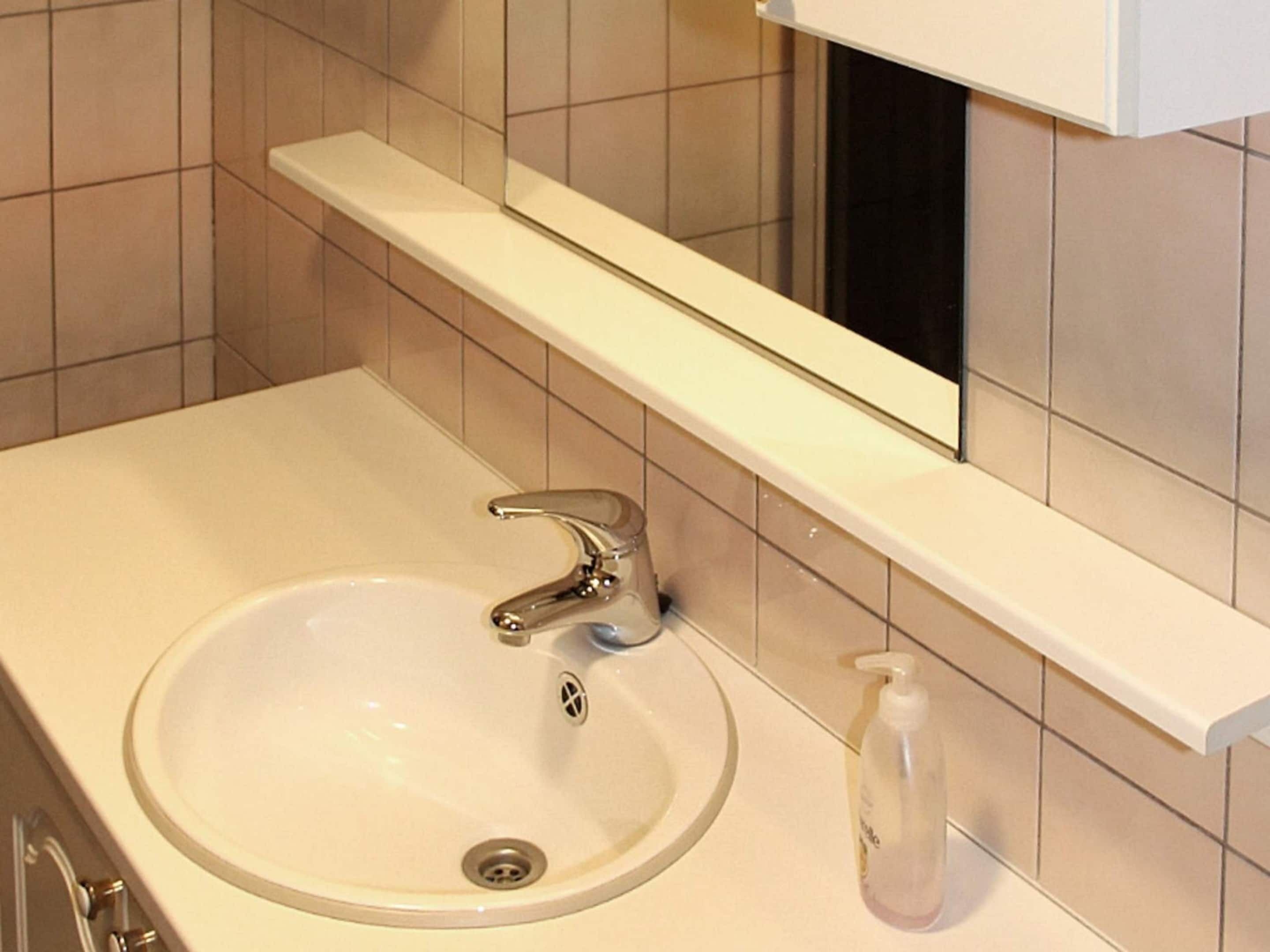 A bathroom with a white sink, chrome faucet, and a mirror above it.