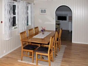 A dining area with a wooden table, chairs, a vase with flowers, and a window with lace curtains.