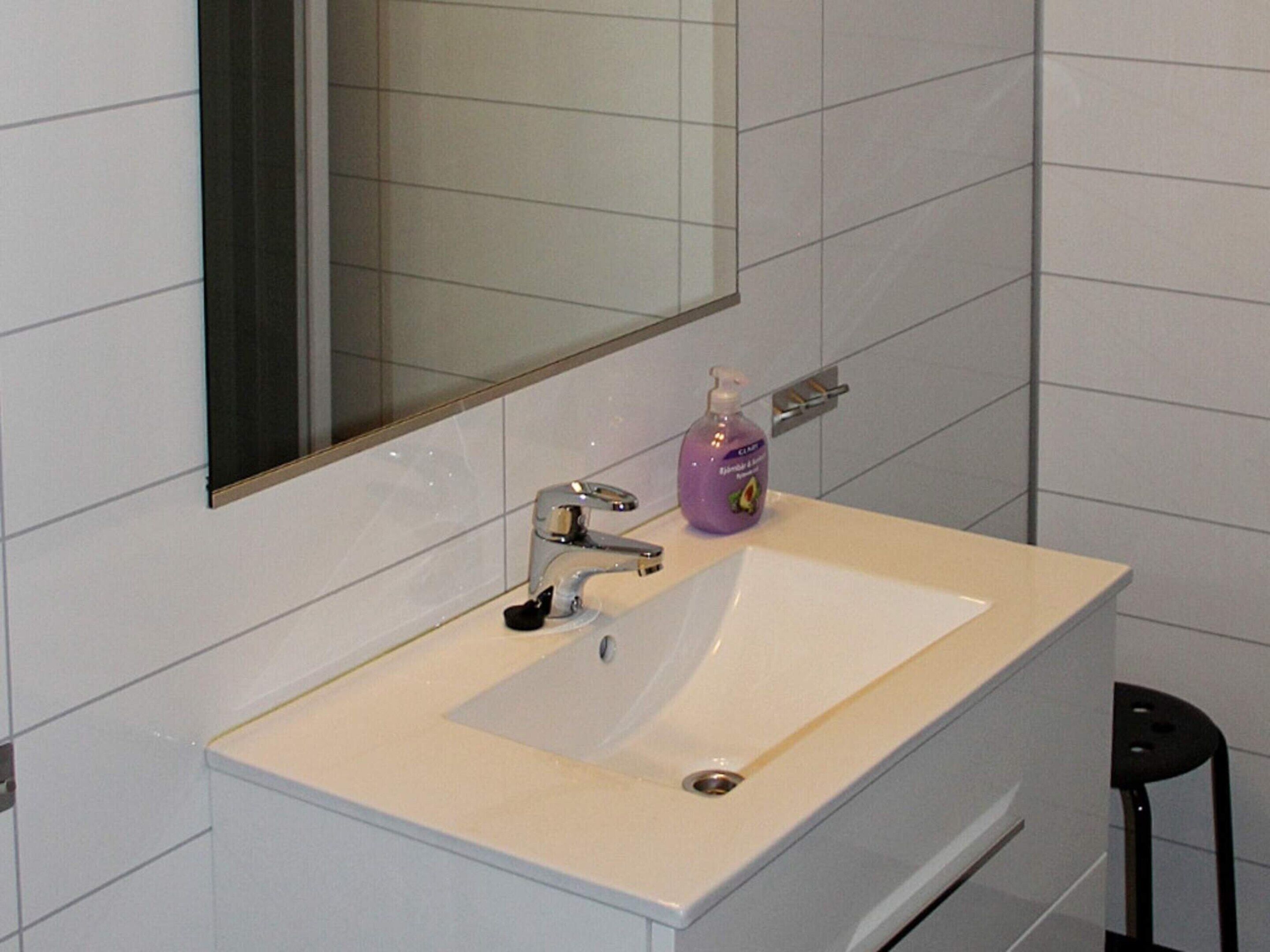 A bathroom with a white sink, a mirror, and a bottle of hand soap.
