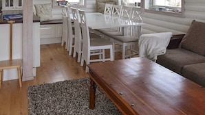 Ein gemütliches Blockhäuschen-Interieur mit einem Holzesstisch, weißen Stühlen, einer Bank und einem Sofa.