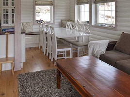 Un interior de cabaña acogedor con una mesa de comedor de madera, sillas blancas, un banco y un sofá.