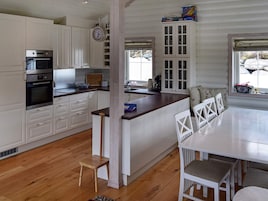Una cocina moderna con armarios blancos, una isla de madera y una zona de comedor con sillas blancas.