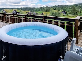 Una piscina inflable sobre una terraza de madera, con vista a casas y follaje al fondo.