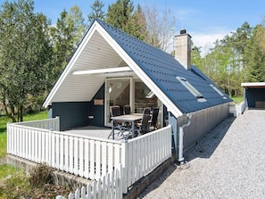 Eine kleine, eingeschossige Holzhütte mit geneigtem Dach und einer überdachten Terrasse.