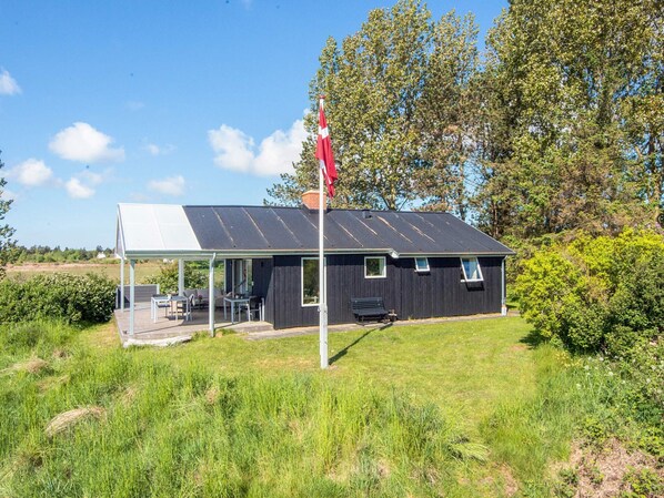 A small building with a covered outdoor seating area, a flagpole, and a grassy landscape.
