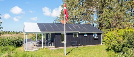 A small building with a covered outdoor seating area, a flagpole, and a grassy landscape.
