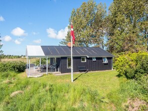En liten byggnad med en överbyggd uteservering, en flaggstång och en grönskande omgivning.