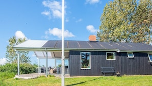 A modern building with a covered patio, a flagpole, and a large tree in the background. - 5 Person Holiday Home in Romo (Rømø)