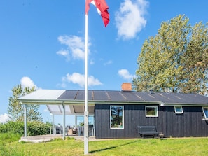 En modern byggnad med en täckt uteplats, en flaggstång och ett stort träd i bakgrunden.