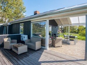 A covered outdoor deck with wicker furniture, a table, and a glass door leading to a garden.