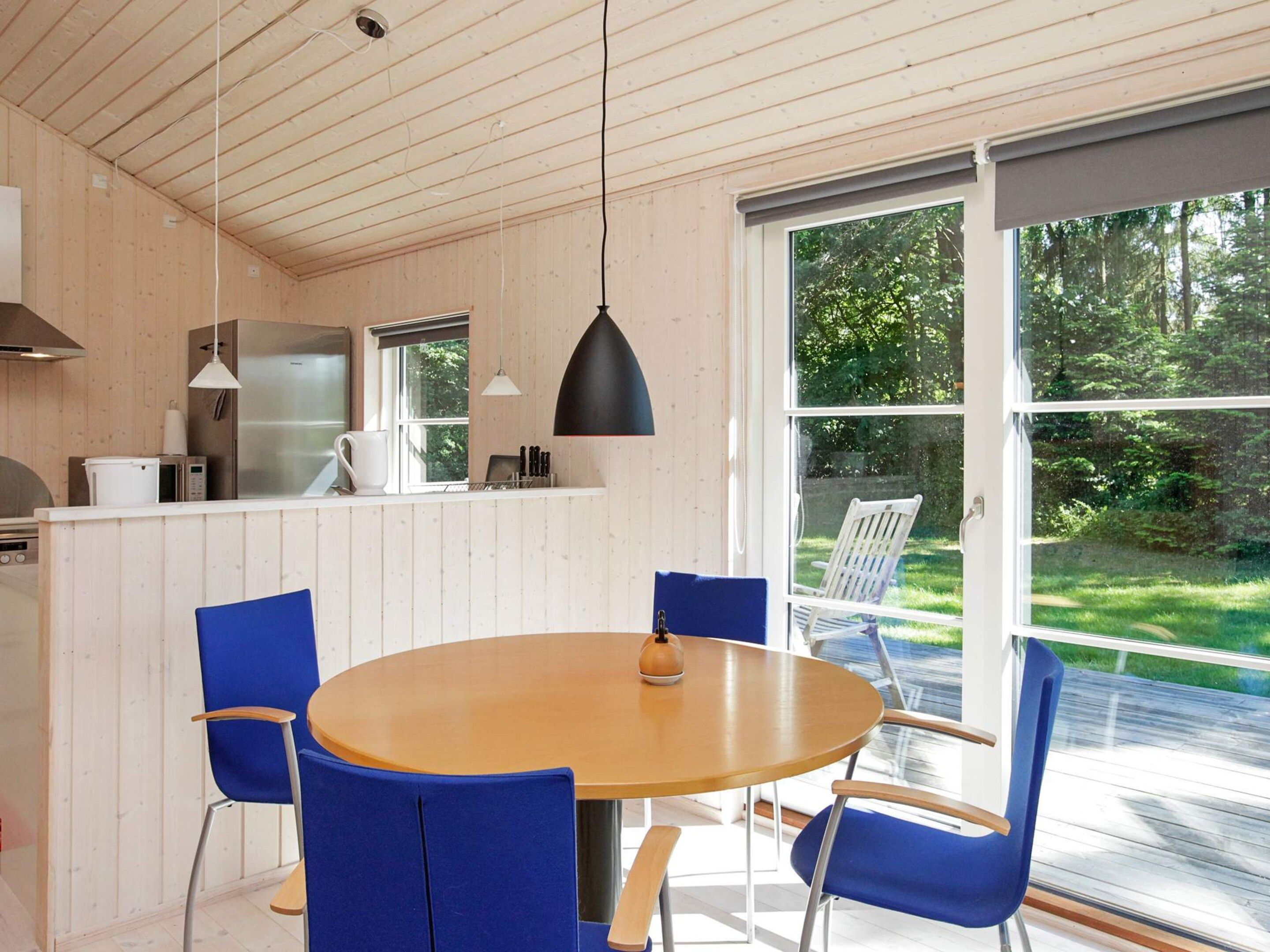 A modern kitchen with a large island, a dining table with blue chairs, and a view of a garden through large windows.