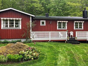 A red wooden house with a white porch and a small garden in front.