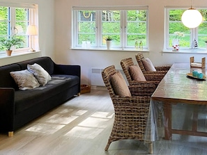A room with a sofa, wicker chairs, a table, and windows with views of greenery.