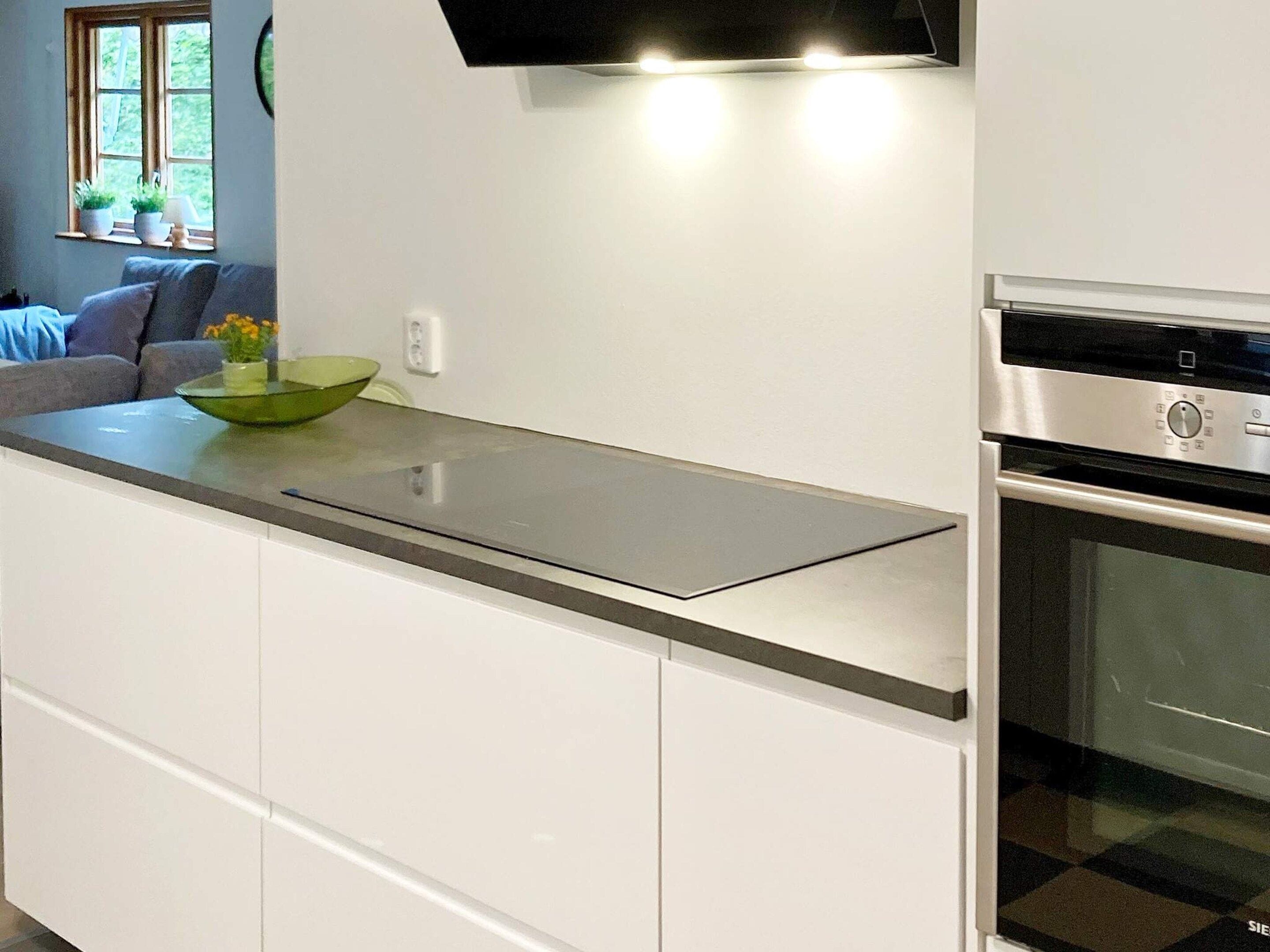 A kitchen with a stainless steel countertop, a built-in oven, and a window with plants.