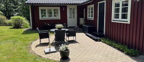 A red building with a patio area featuring a table and chairs, surrounded by greenery.