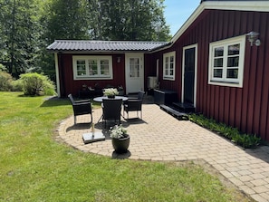 A red building with a patio area featuring a table and chairs, surrounded by greenery. - Holiday Home in HÃ¤stveda (Hästveda)