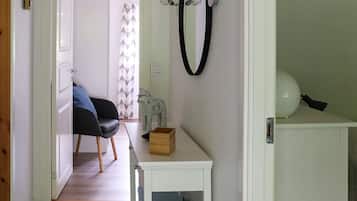 A room with a bed, a chair, a small table with a box, a wall-mounted light fixture, and a door leading to another room.