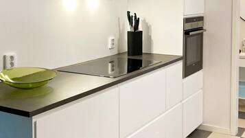 A modern kitchen with white cabinets, a black countertop, and a green glass bowl. There is a knife block on the countertop and an oven built into the cabinetry.