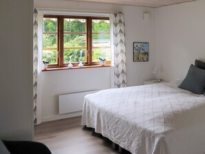 A bedroom with a large bed, a window with curtains, a radiator, and a small table with a lamp.