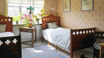 A room with two wooden beds, a window with plants, a radiator, and patterned wallpaper.