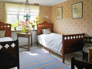 A room with two wooden beds, a window with plants, a radiator, and patterned wallpaper. - 7 Person Holiday Home in Varekil (Varekil)