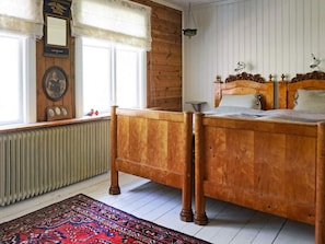 A wooden bed with a headboard, a radiator, a window with a curtain, and a patterned rug. - 7 Person Holiday Home in Varekil (Varekil)