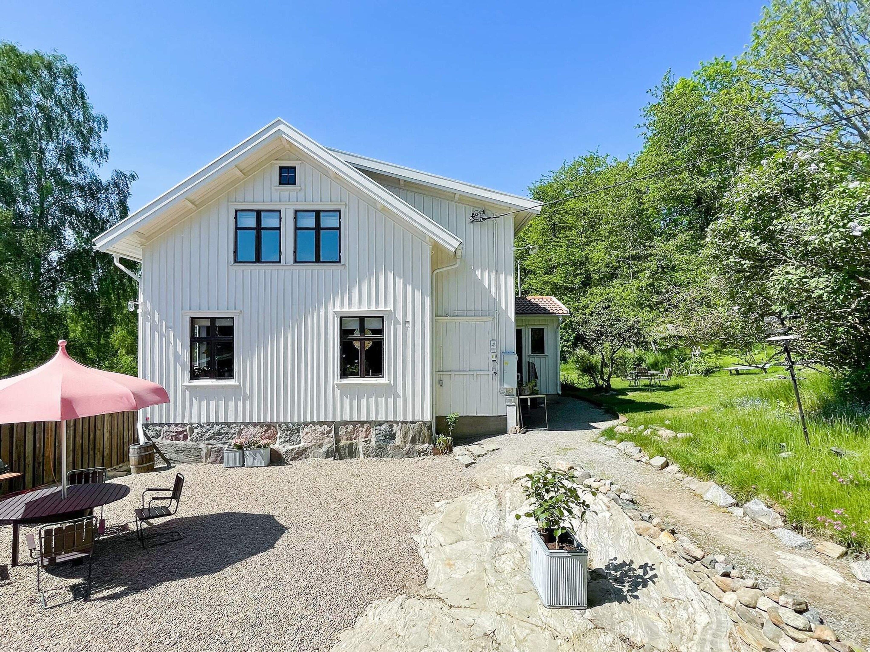 A white house with a gravel driveway, a patio with a table and chairs, and a small garden area.