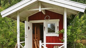 A rustic cabin with a white exterior, a wooden deck, and a small window. - 6 Person Holiday Home in Savsjo (Savsjo)