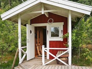 A rustic cabin with a white exterior, a wooden deck, and a small window. - 6 Person Holiday Home in Savsjo (Savsjo)