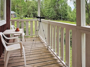 A wooden deck with a telescope on a tripod, white plastic chairs, and a table with a clay pot.