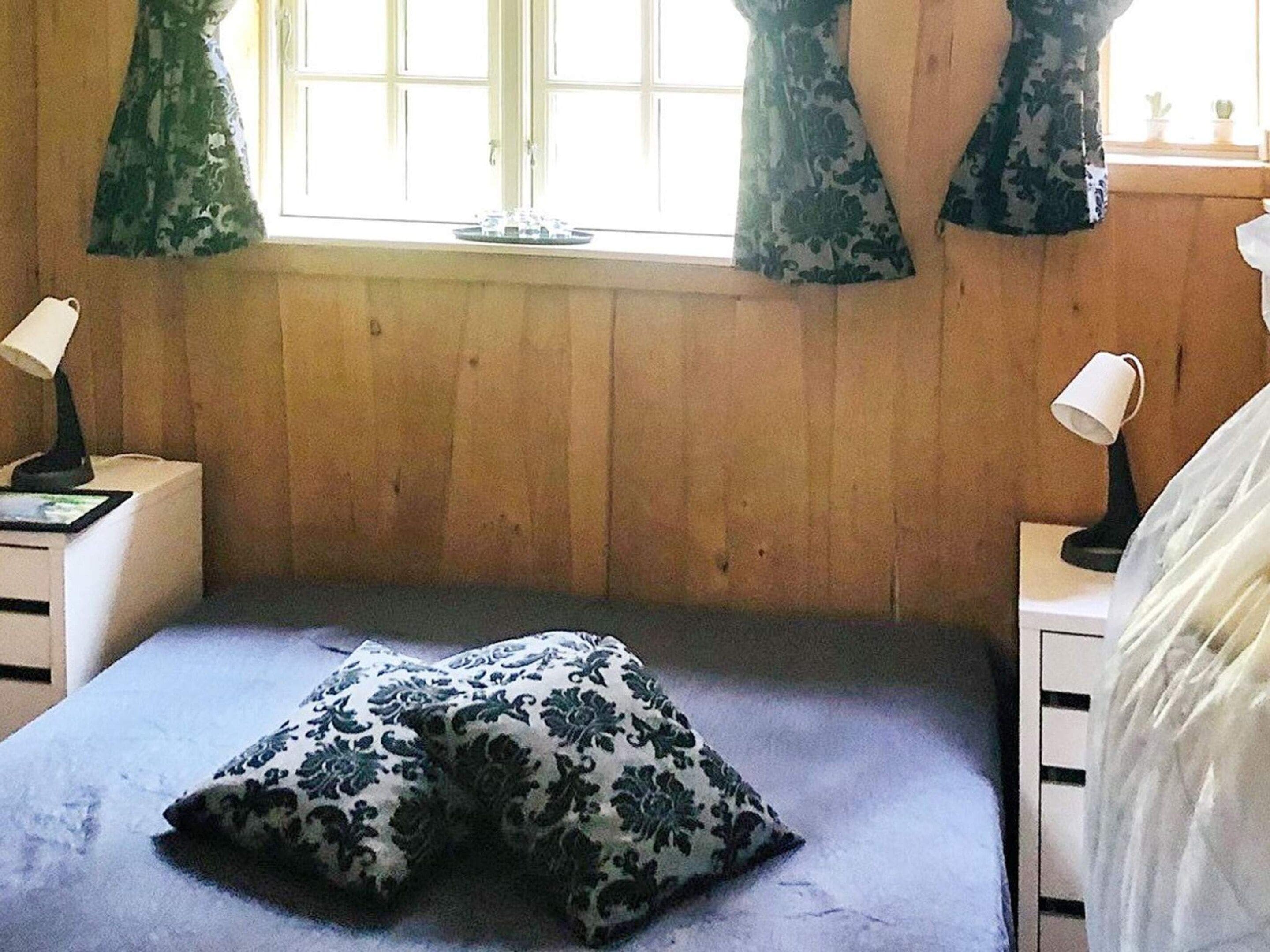 A bedroom with a single bed, two bedside tables, and a window with curtains.