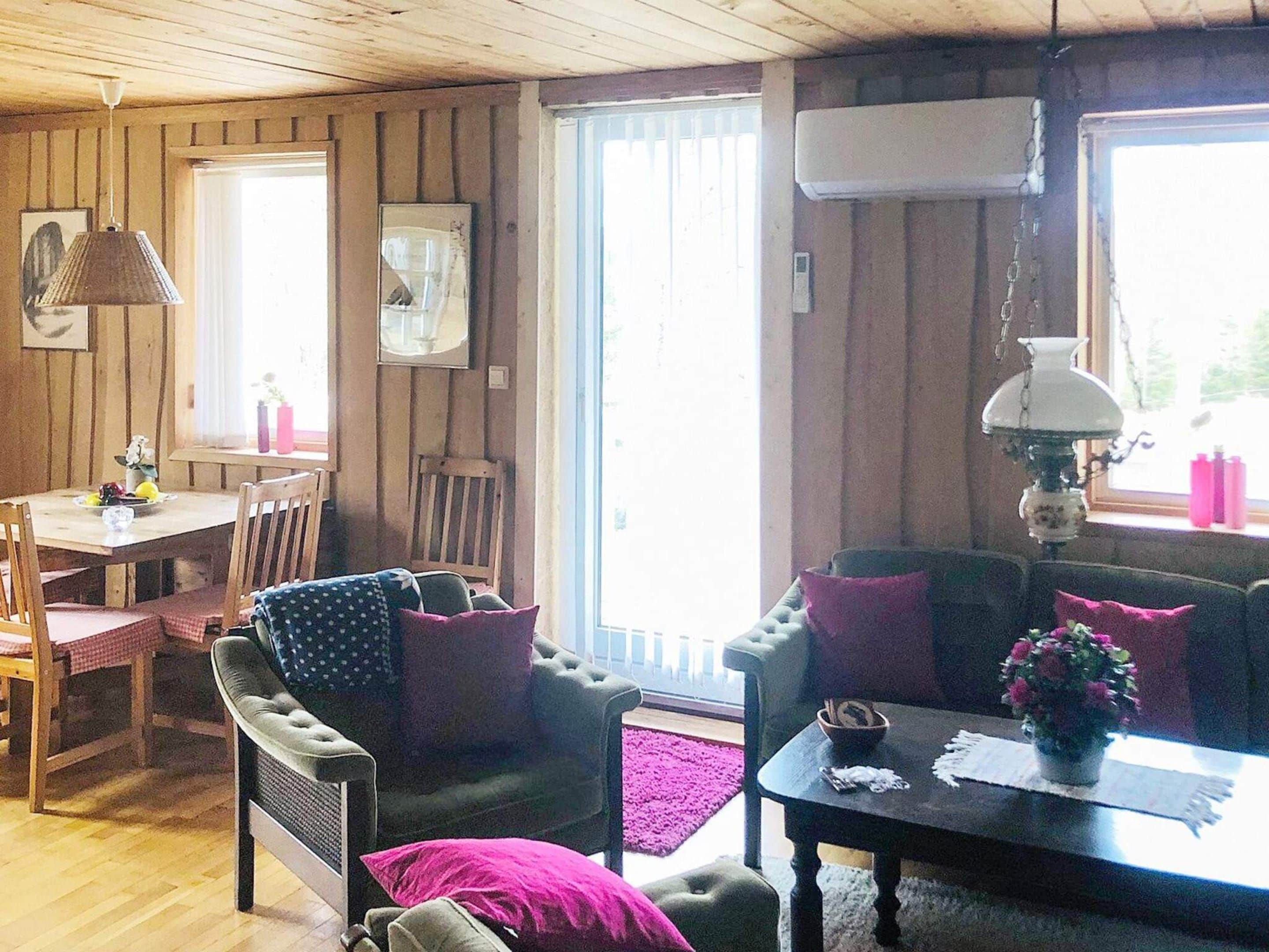 A cozy cabin interior with a dining area, a sofa set, and a table with a vase of flowers.